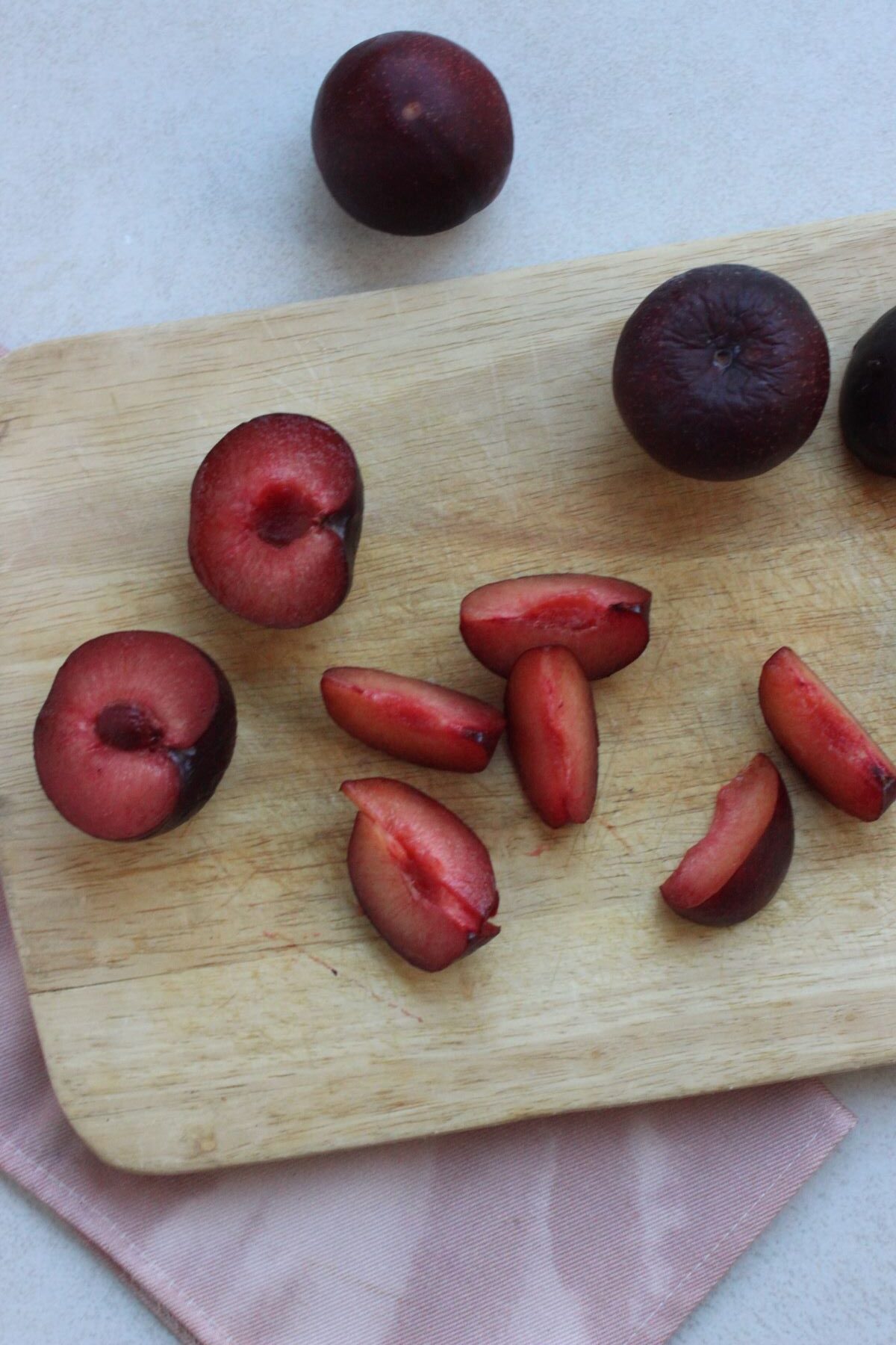 Plums, plums cut in half, and sliced plum on a wooden board.