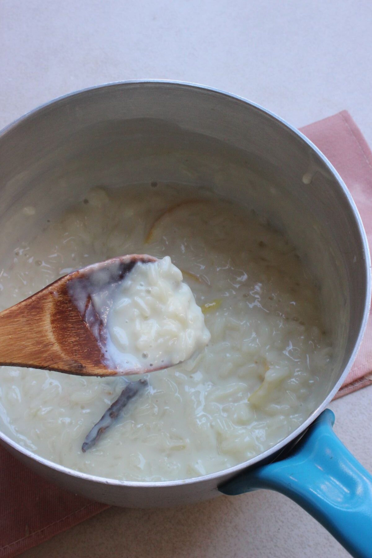 A deep saucepan with rice pudding, and a wooden spoon with rice pudding.