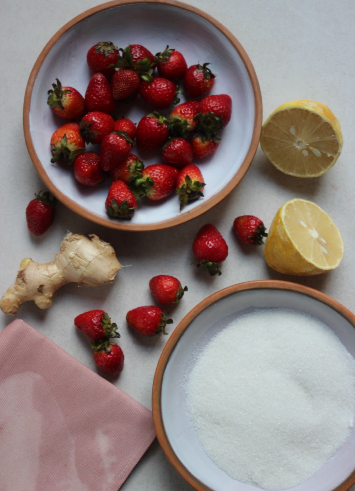 Strawberry and ginger jam ingredients on a white surface seen from above.