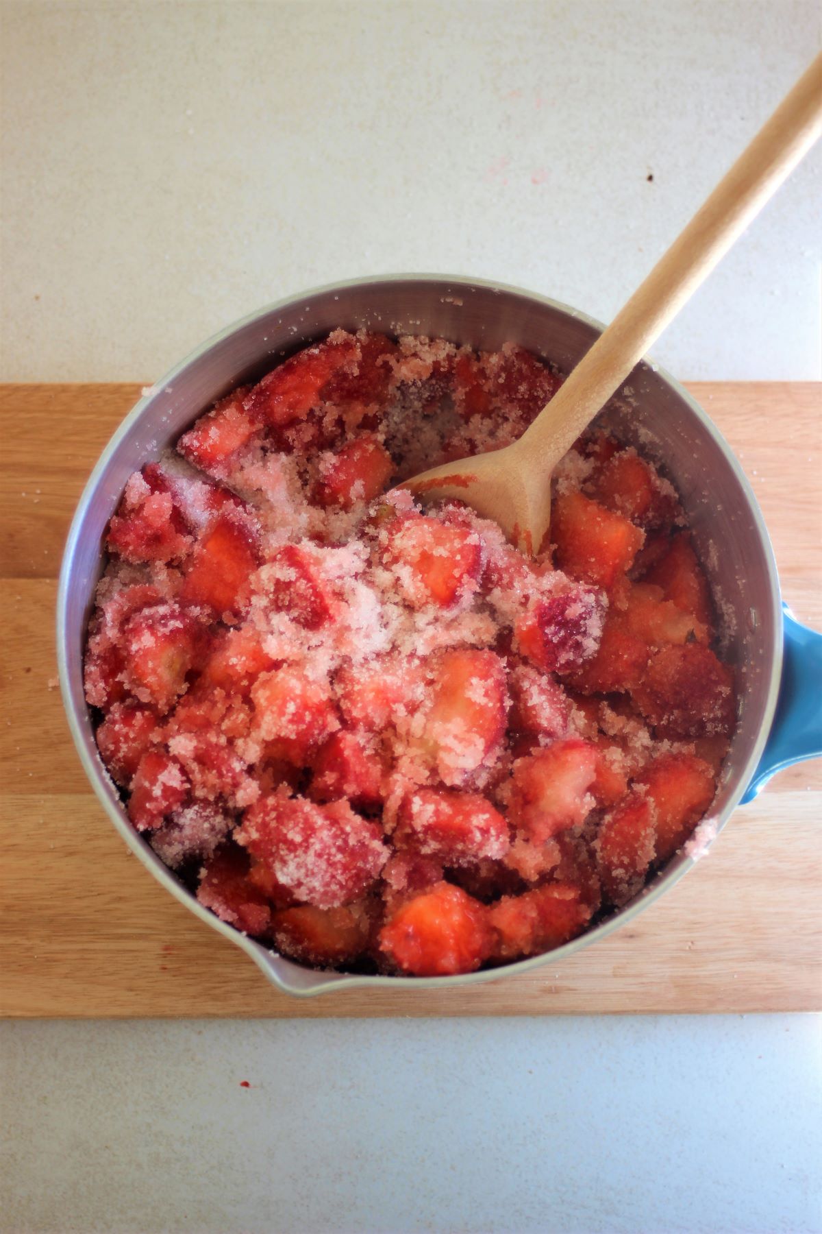 A deep saucepan with chopped strawberries and sugar, and a wooden spoon..