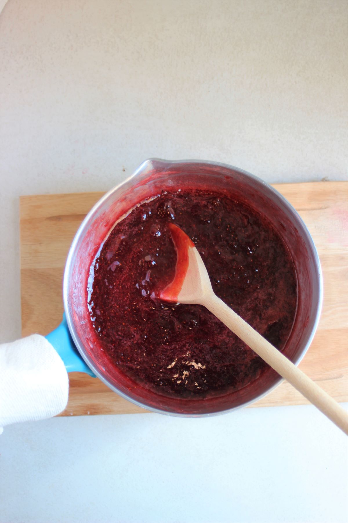Deep saucepan with strawberry jam and a wooden spoon.
