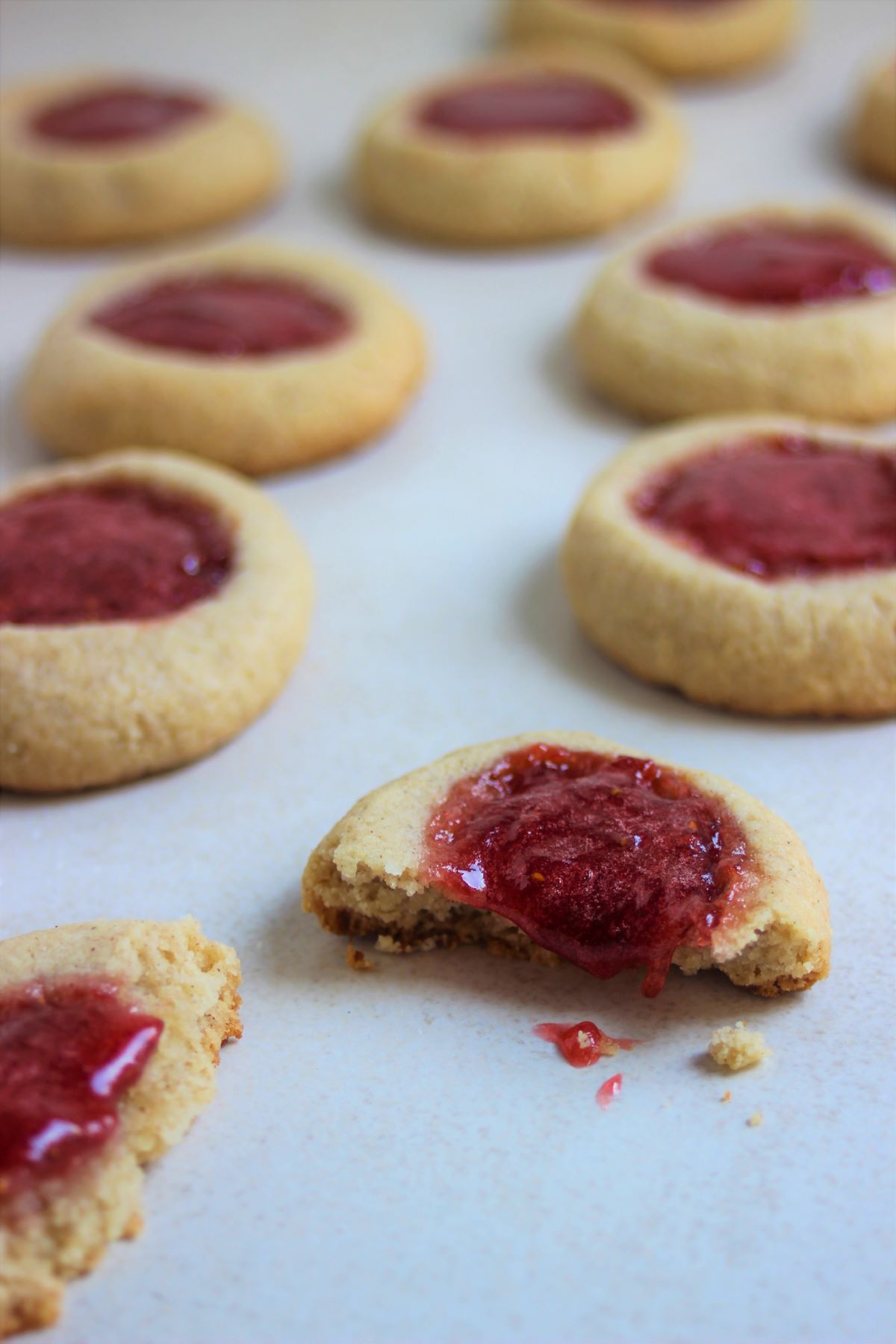 Many thumbprint cookies, one has broken and the strawberry jam falls off.