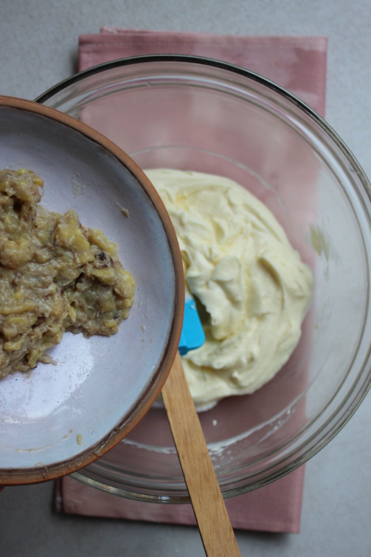 Plate with mashed bananas is about to be poured into a glass bowl with cream.