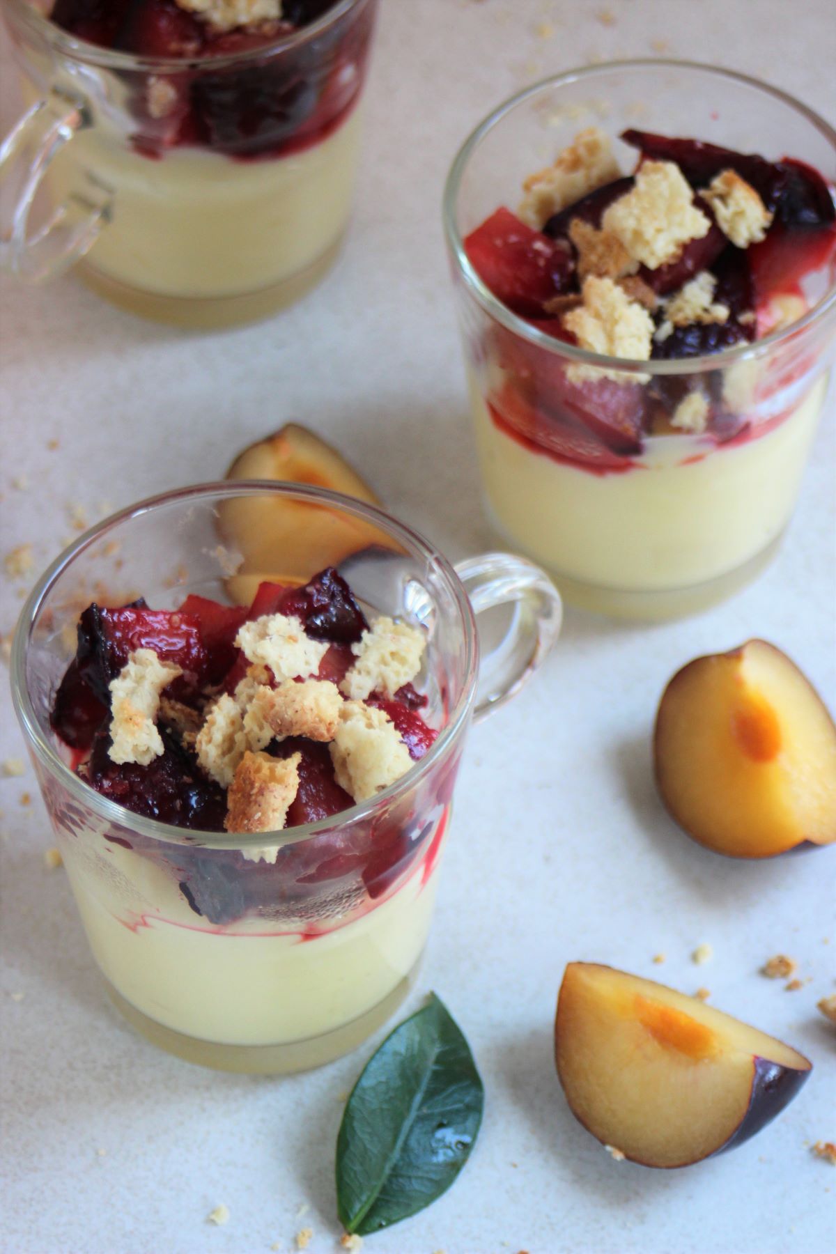 Glass jars with cream, plum compote, and crumbs. Slices of plums on the side.