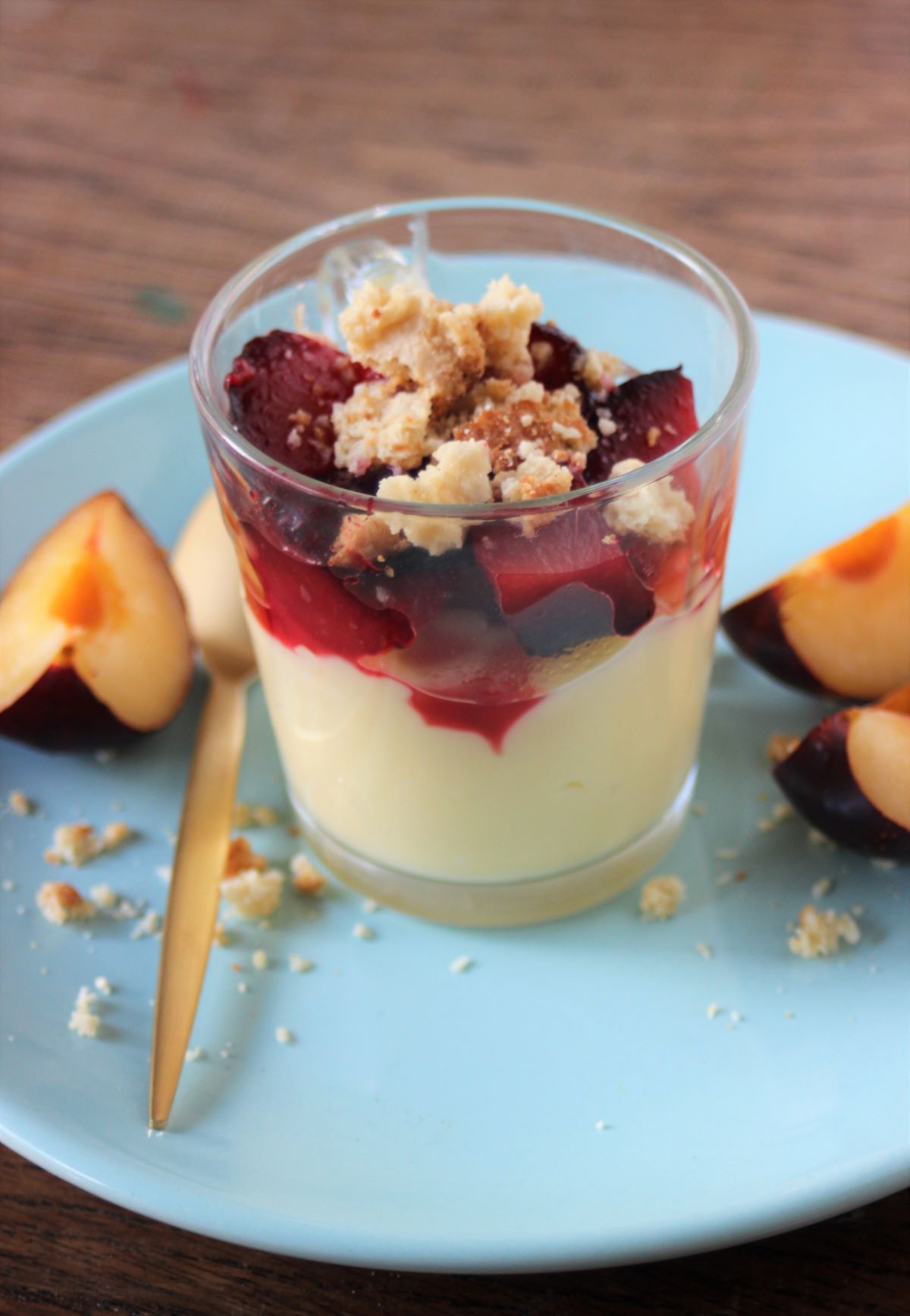 Glass cup with cream, plum compote, and crumbs. Slices of plums on the side.