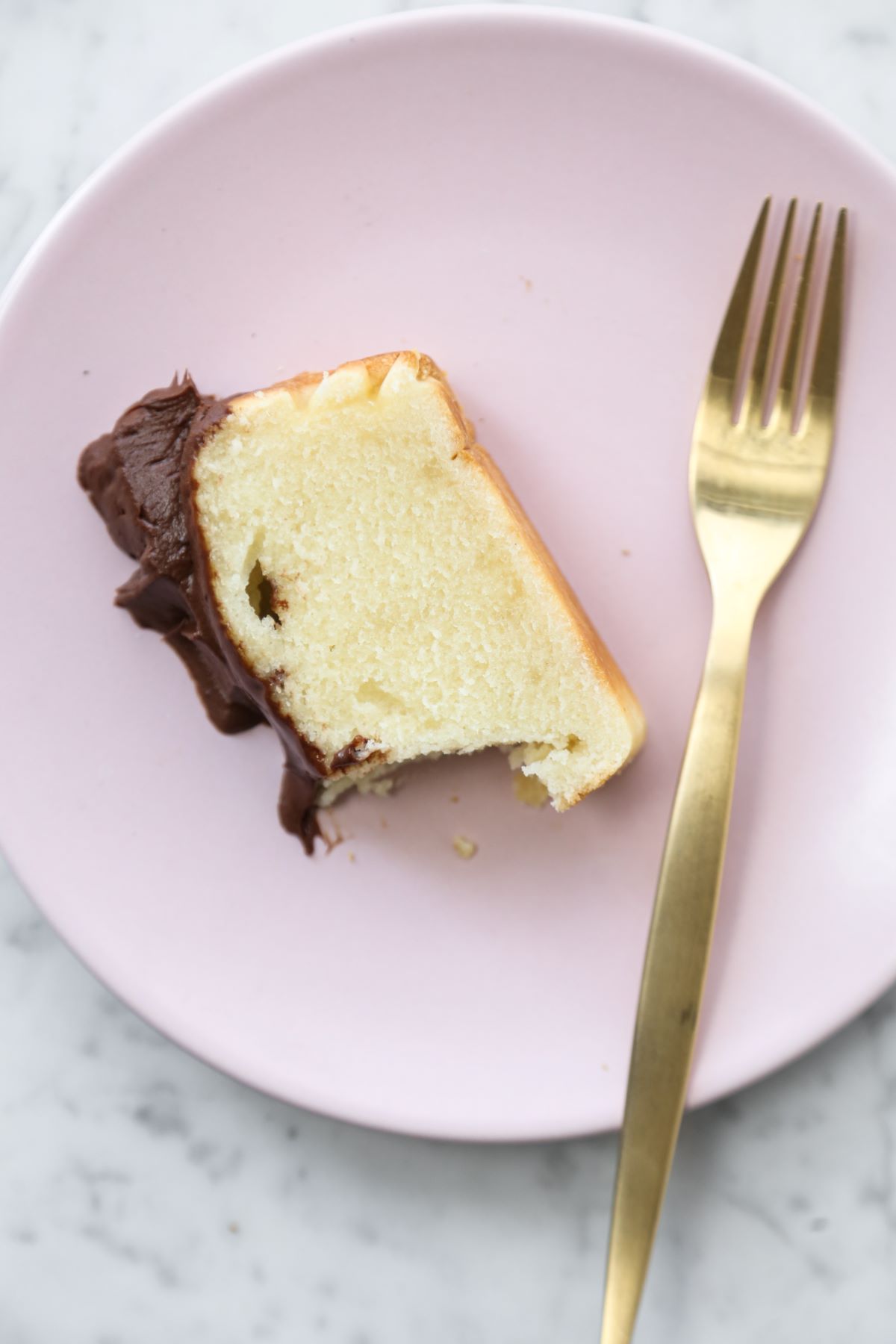 Slice of vanilla loaf cake with chocolate ganache on a pink plate and a gold fork.