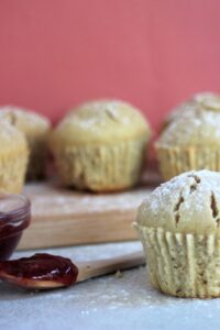 Vanilla muffins and a spoon with red jam. Many muffins behind, on a wooden board.