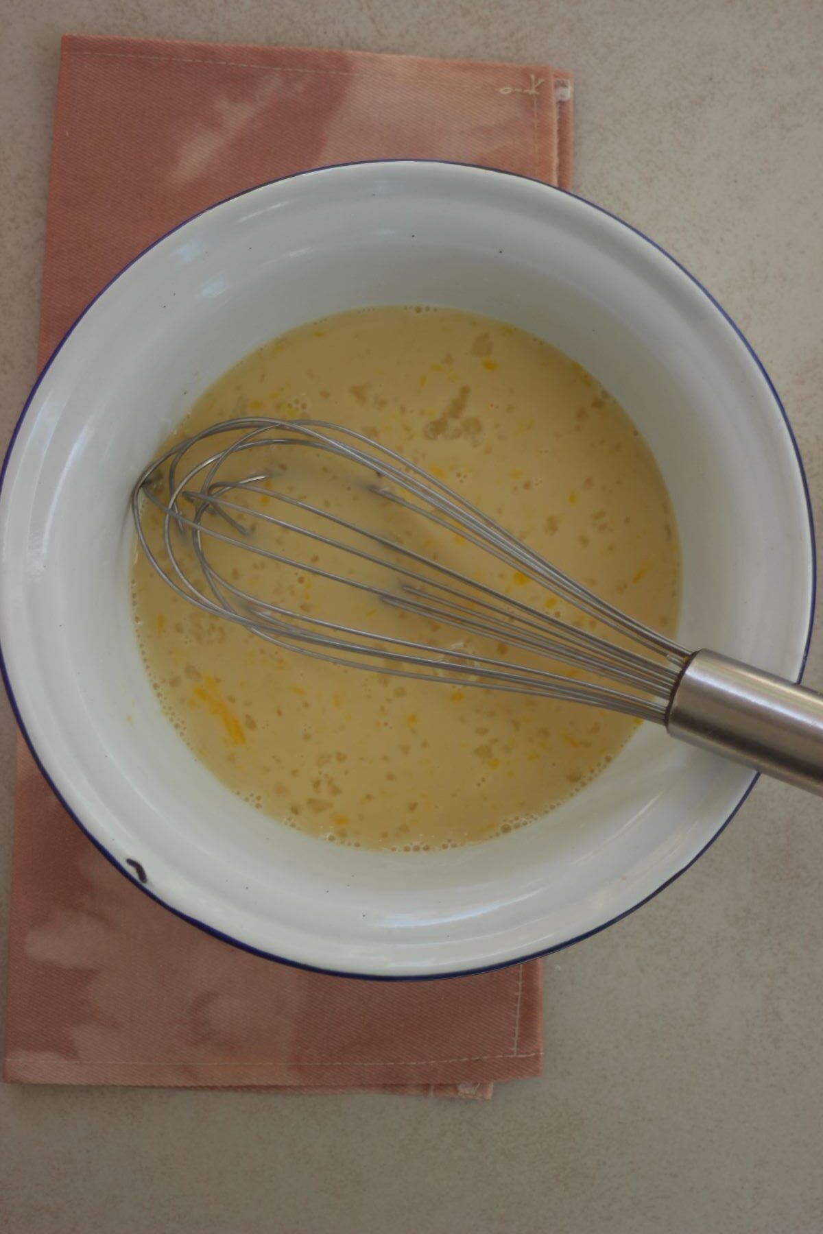 A bowl with a yellow liquid and a hand whisk.
