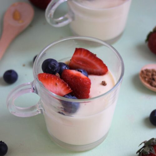 Glass cup with vanilla panna cotta, strawberries, and blueberries.