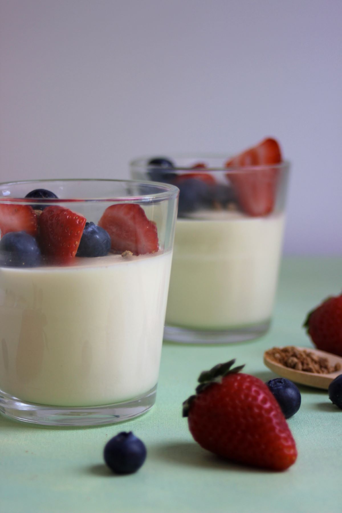 Glass cup with vanilla panna cotta, strawberries, and blueberries. Another cup behind.