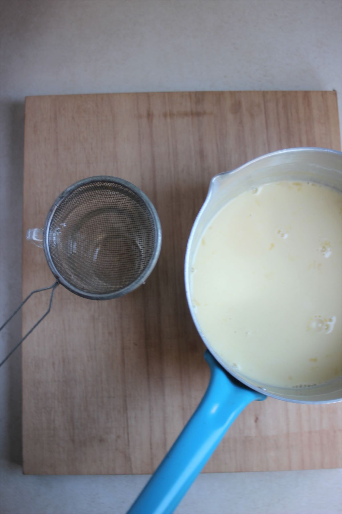 Deep saucepan with milk and a strainer on the side, on a wooden board.