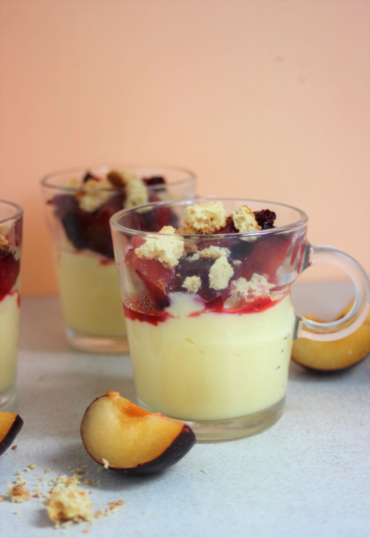 Glass cups with cream, plum compote, and crumbs. Slices of plums on the side.