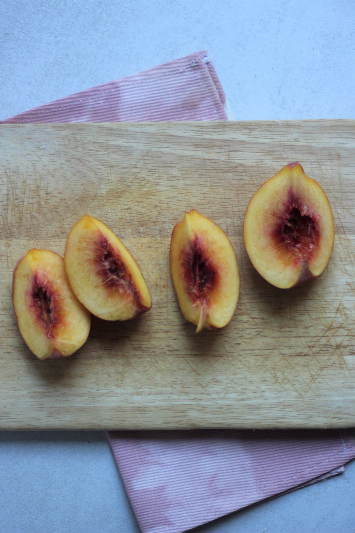 Four peach quarters on a wooden board.