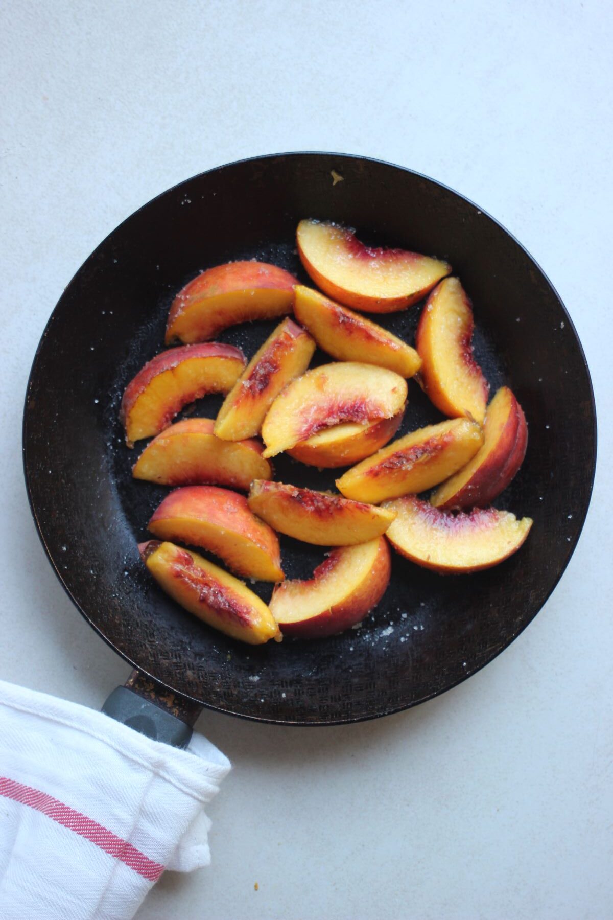 A skillet with sliced peaches. A dish towel on the handle.