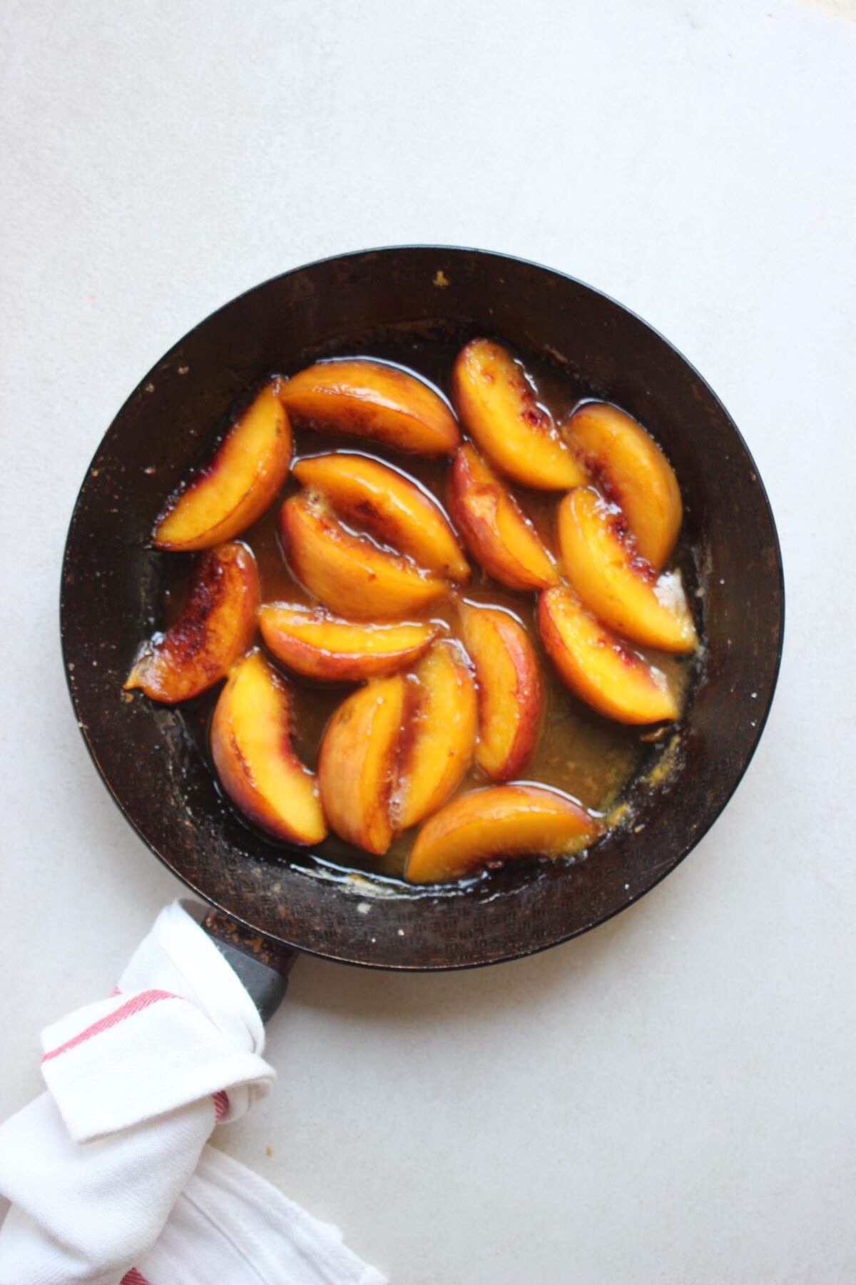 A skillet with sliced peaches and liquid. A dish towel on the handle.