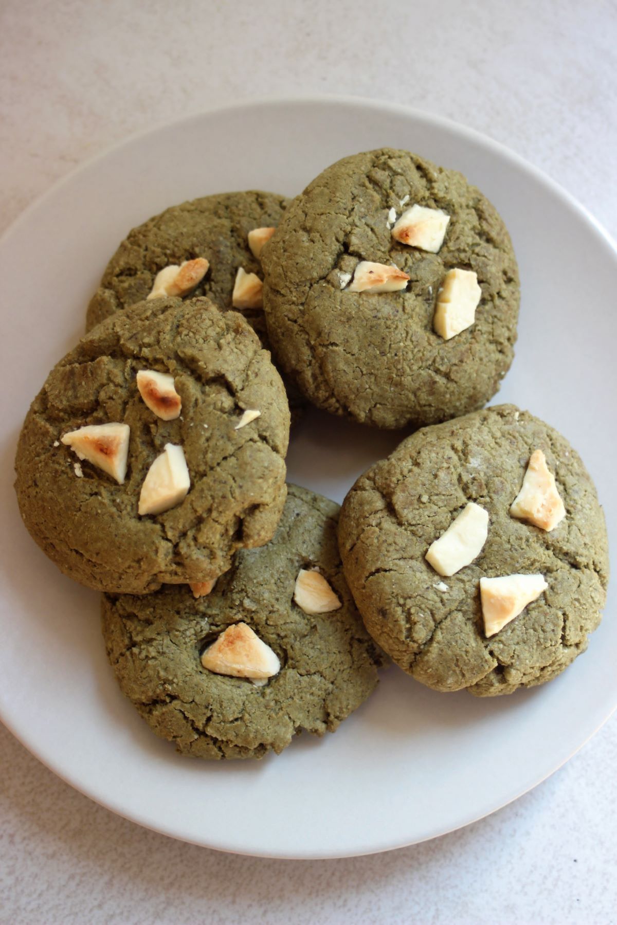 Many matcha cookies with white chocolate chunks on a white plate.