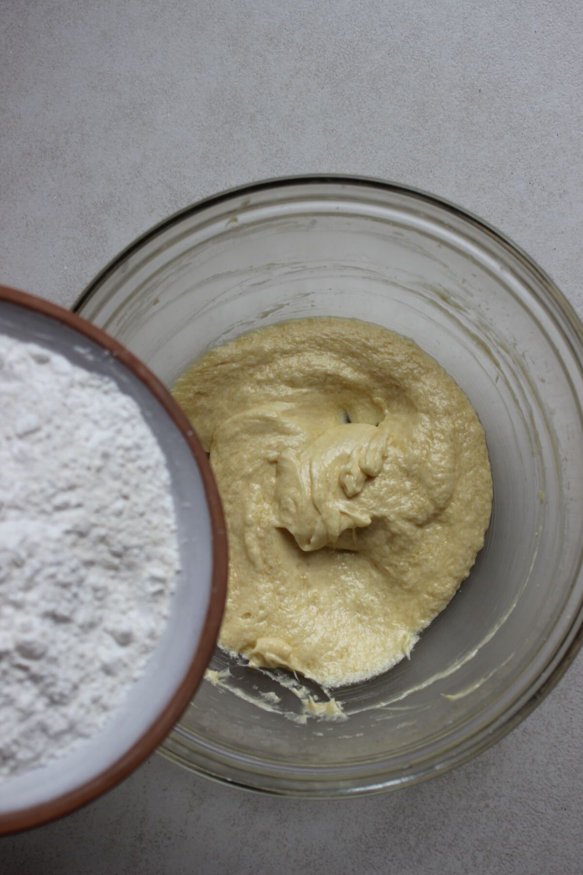 A plate with flour is about to be poured into a glass bowl with a mixture.