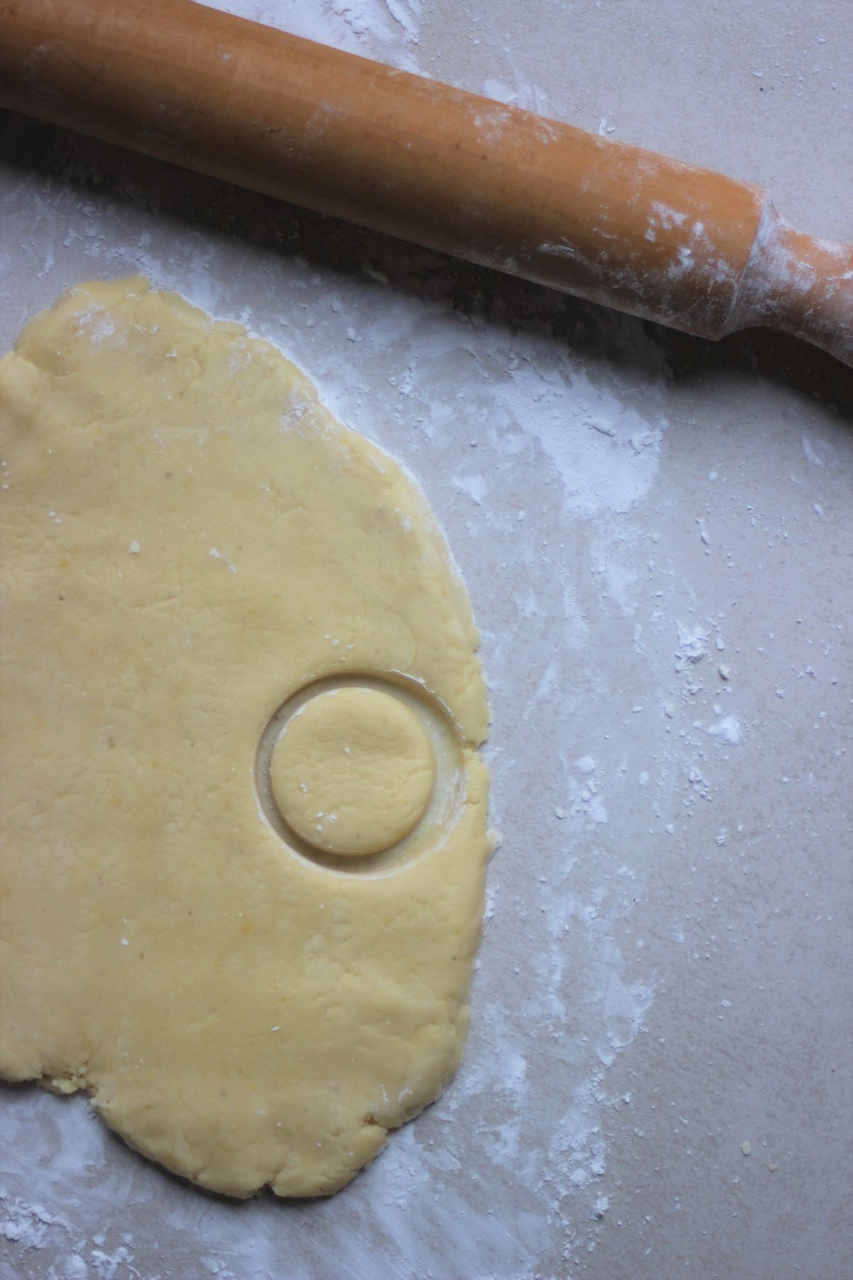 A stretched dough on a white surface with a cut roundel and a rolling pin.