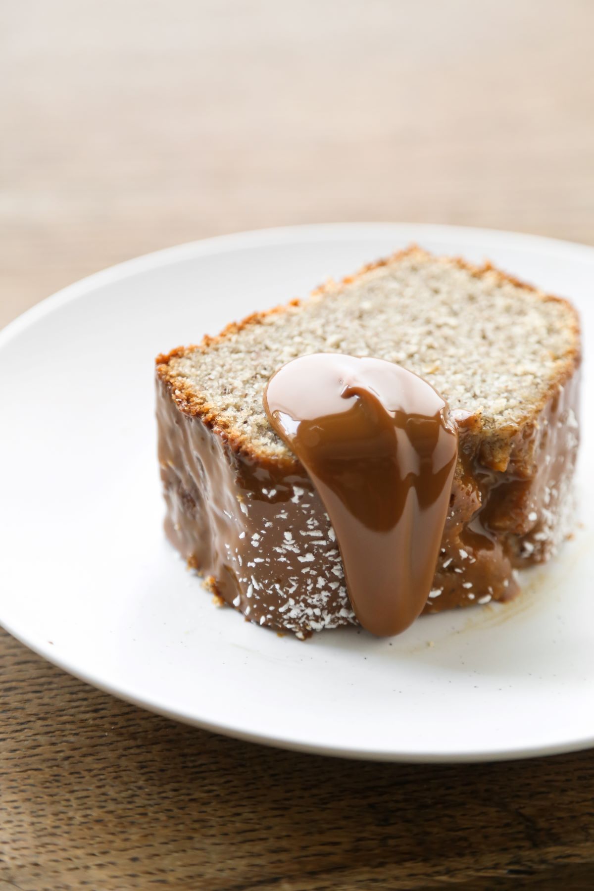 Slice of banana loaf cake with dulce de leche falling down, on a white plate.