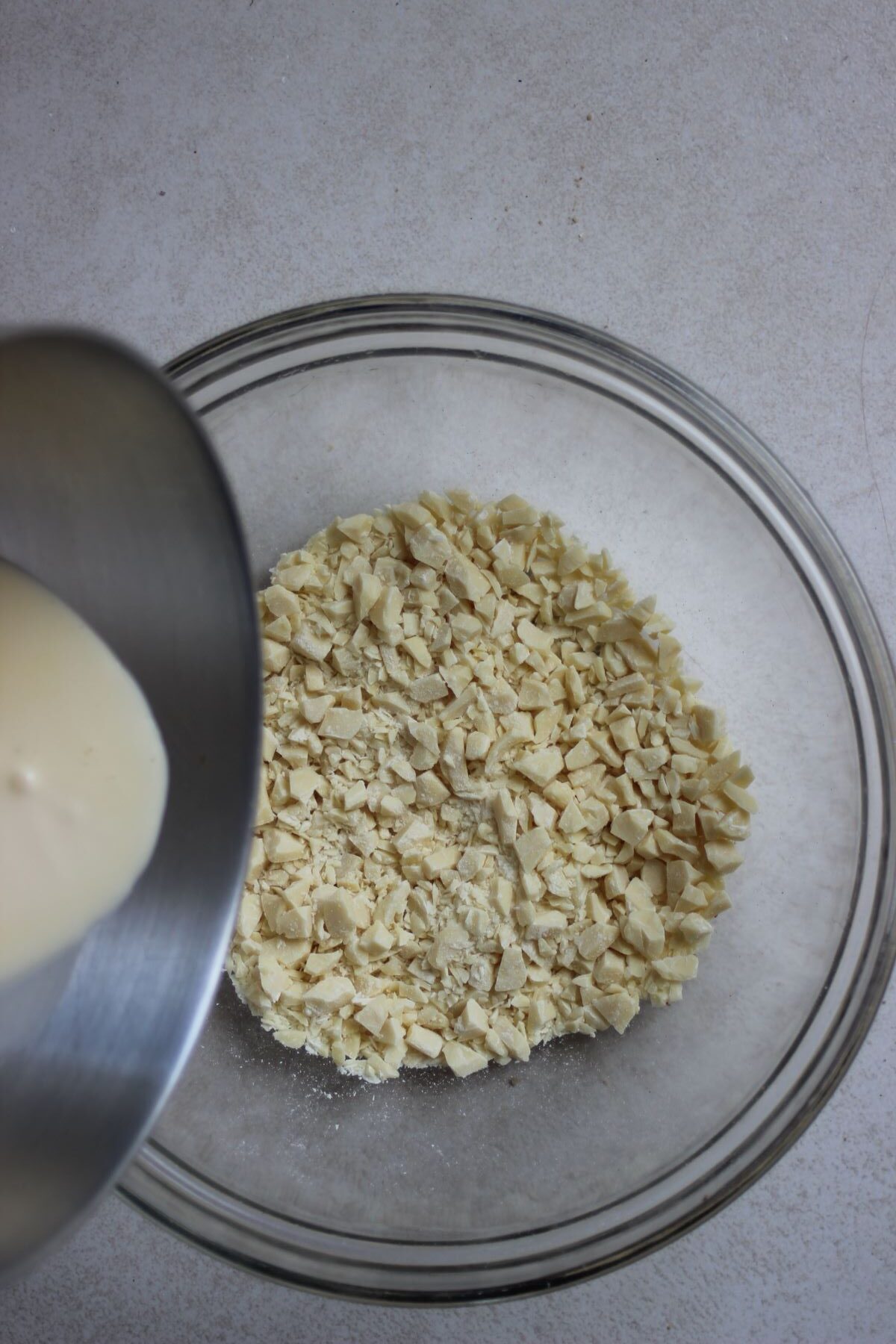 Saucepan with cream is about to be poured into a bowl with finely chopped white chocolate.