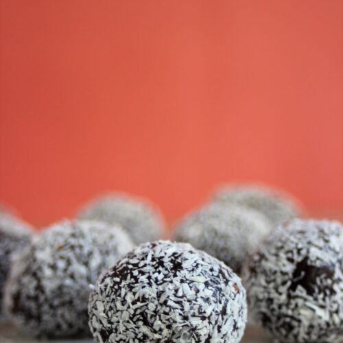 Brigadeiros with shredded coconut on a white surface and pink background.
