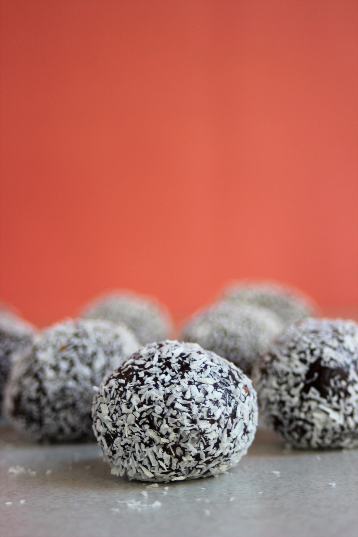 Brigadeiros with shredded coconut on a white surface and pink background.