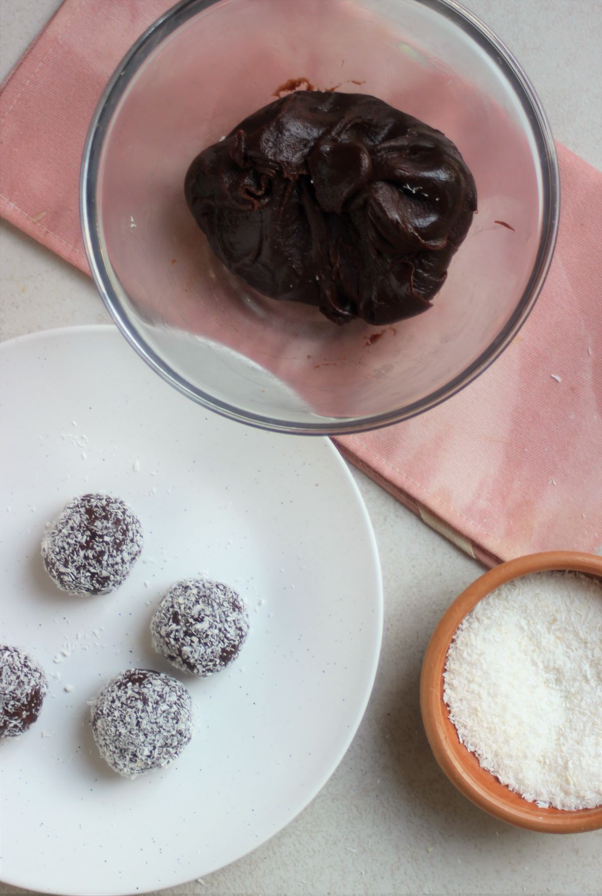Glass bowl with a big chocolate ball, a white plate with brigadeiros, and bowl with shredded coconut.