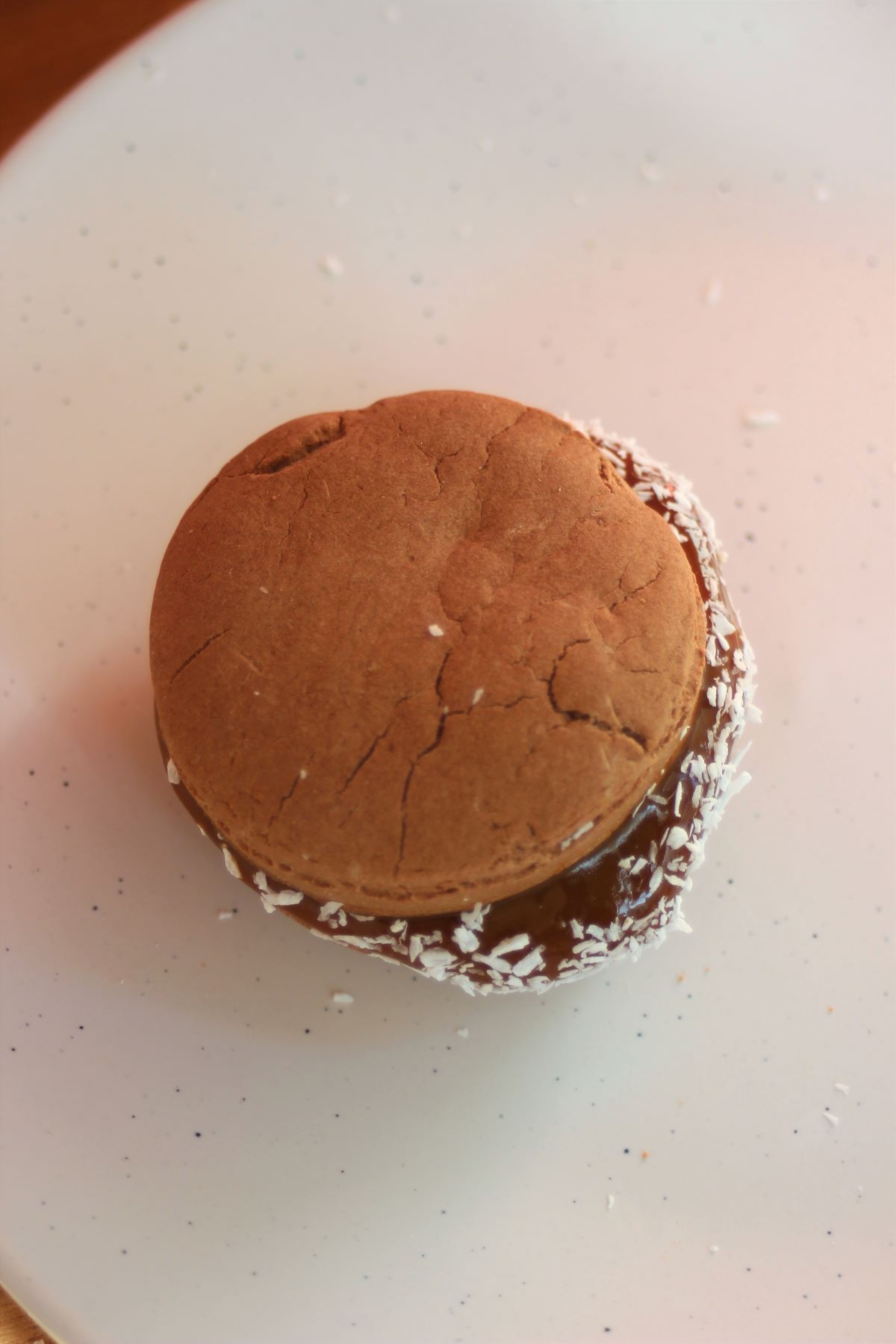 A chocolate alfajor with dulce de leche on a white plate seen from above.