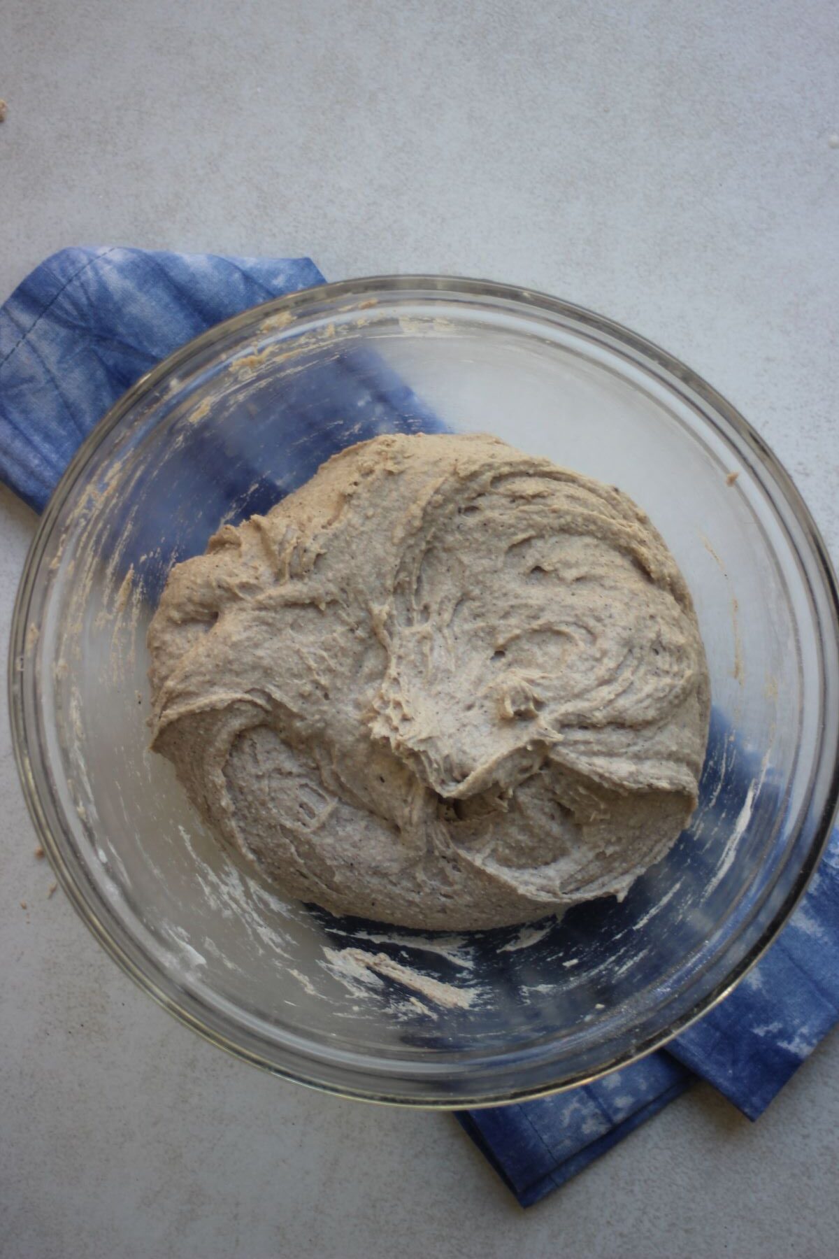 A glass bowl with a sticky bread dough. Blue napkin under the bowl.