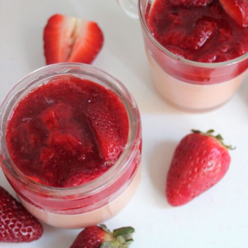 Two glass jars with strawberry panna cotta and strawberry sauce. Fresh strawberries on the side.