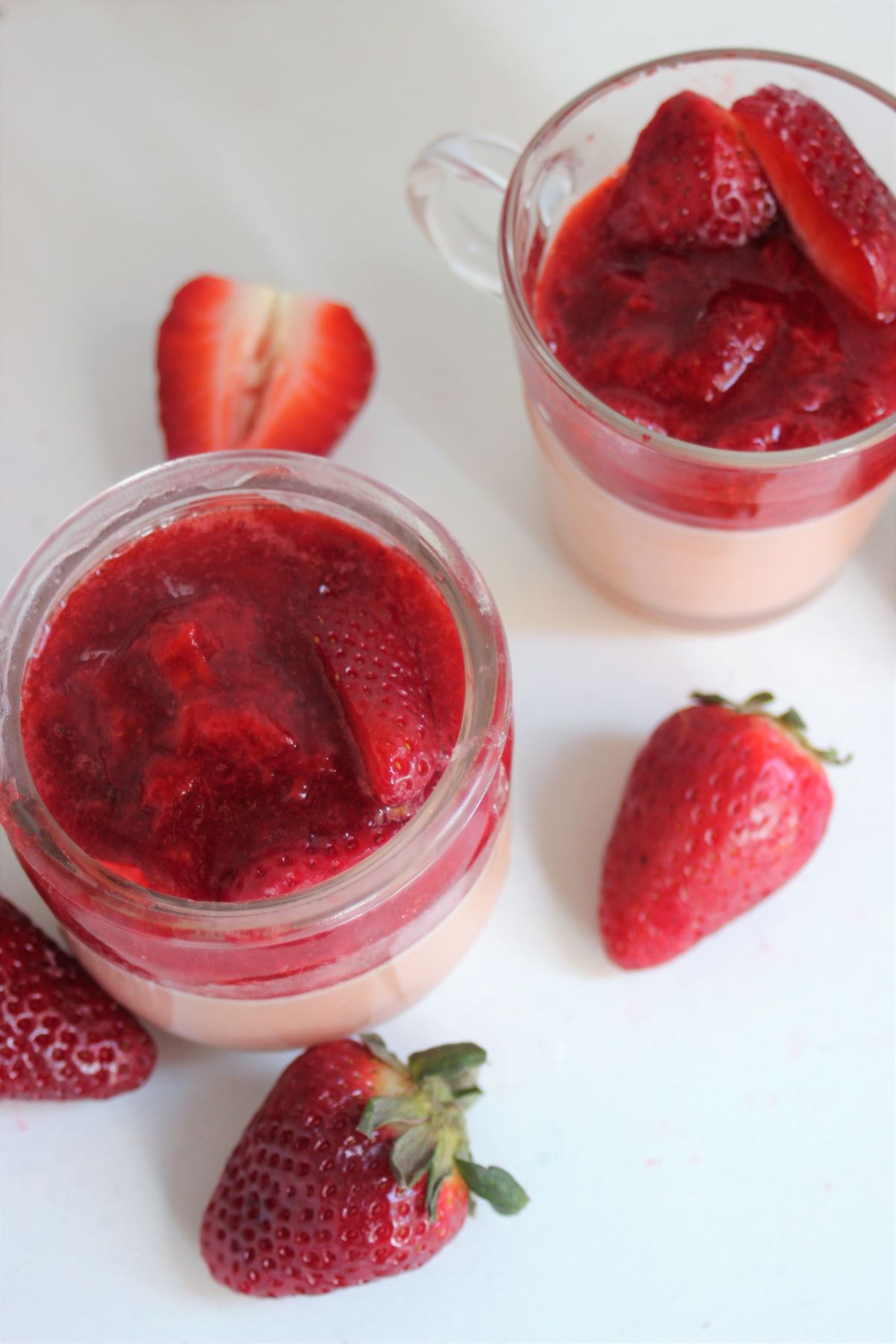 Two glass jars with strawberry panna cotta and strawberry sauce. Fresh strawberries on the side.