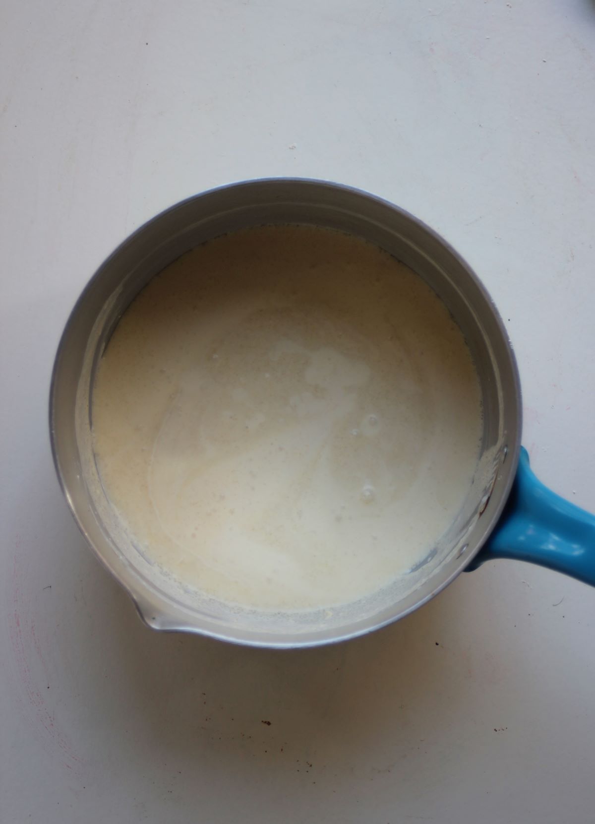 A deep saucepan with cream on a white surface.