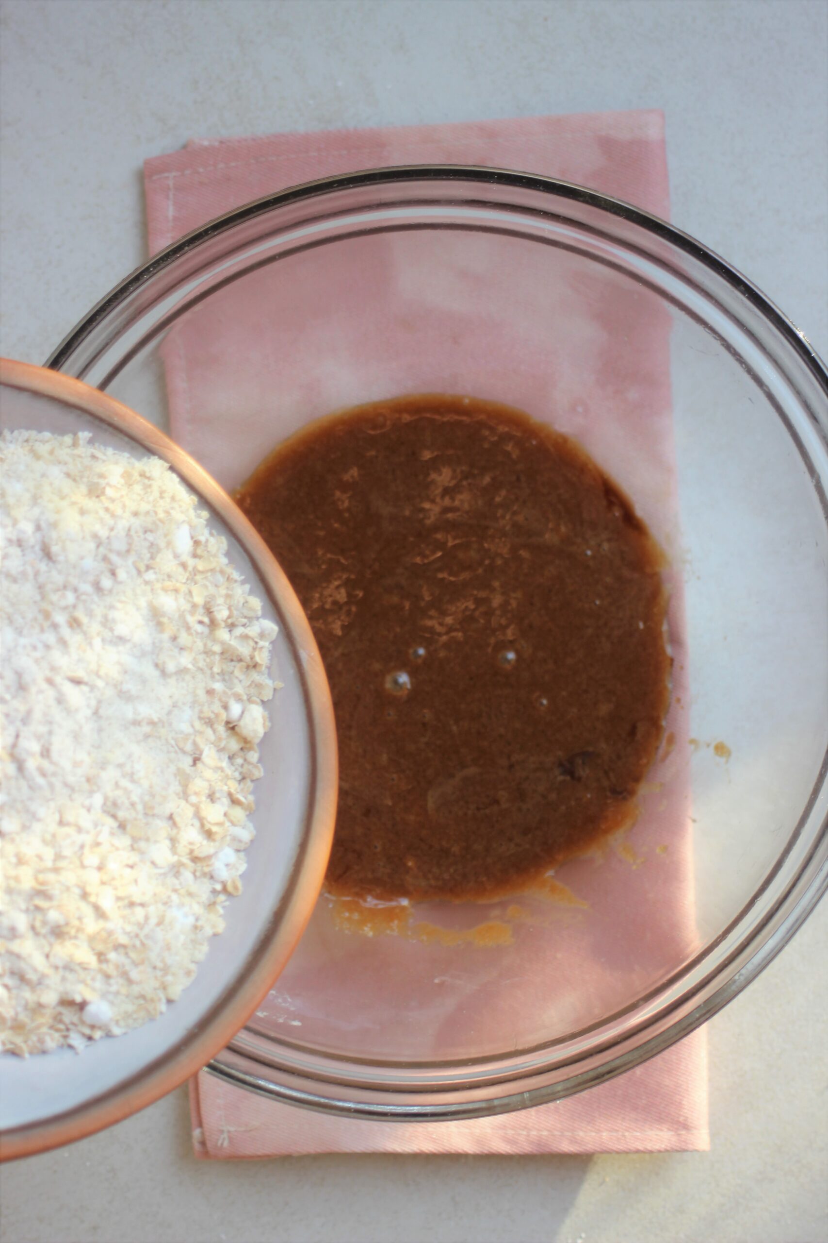 A plate with flour is about to be poured into a glass bowl with brown mixture.