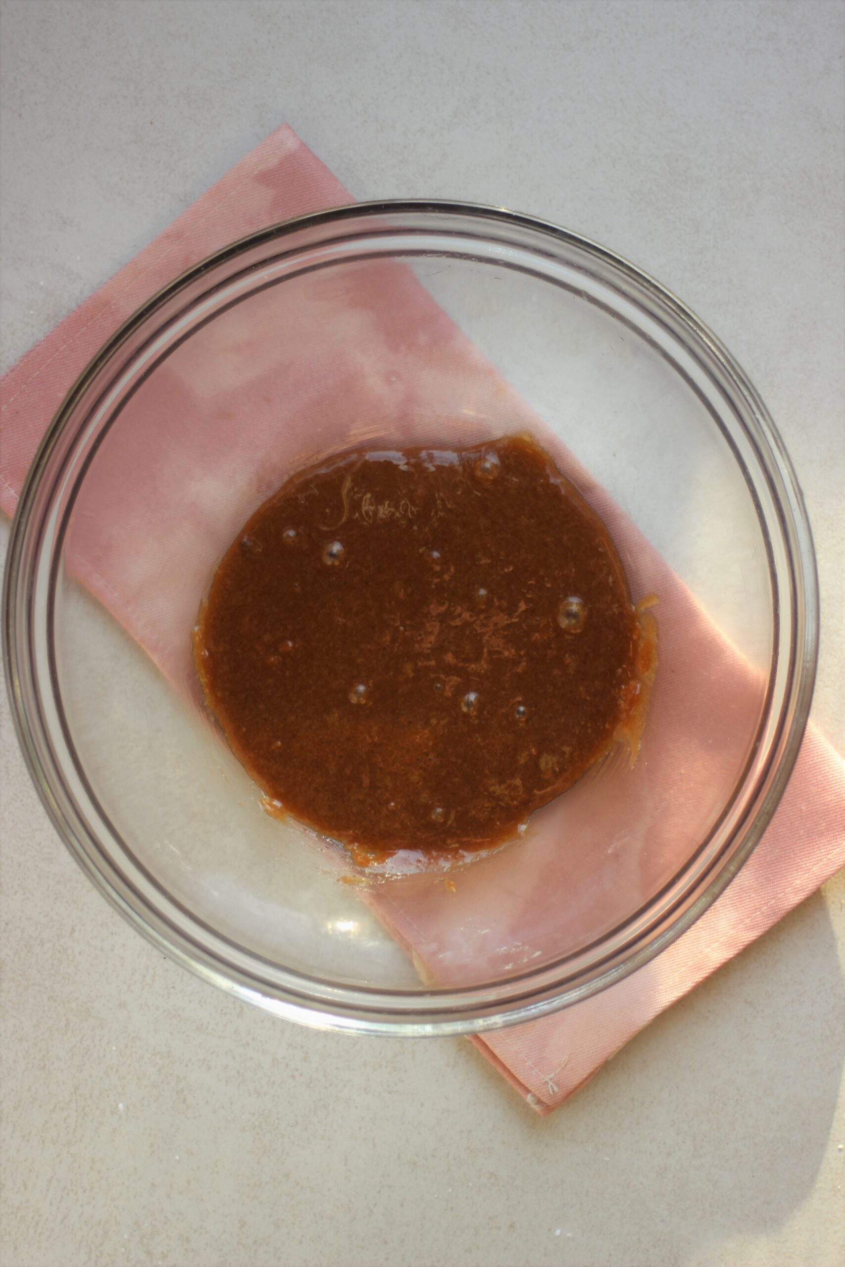 Glass bowl with a brown mixture. Pink napkin under the bowl.
