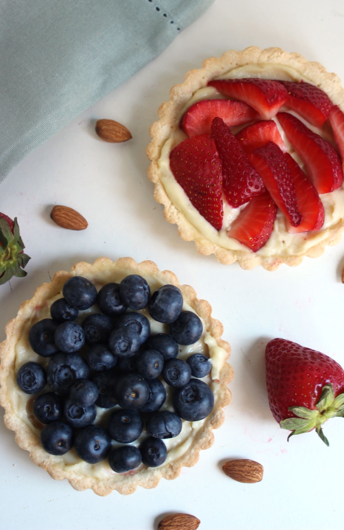 A strawberry and a blueberry tart seen from above. Fresh strawberries and almond on the sides.
