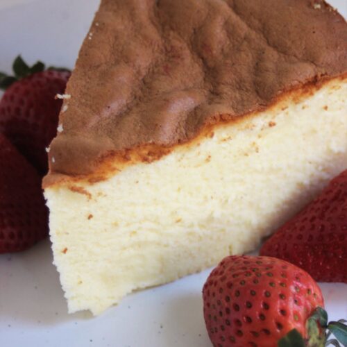 A piece of japanese cheesecake on a white plate. Strawberries on the side.