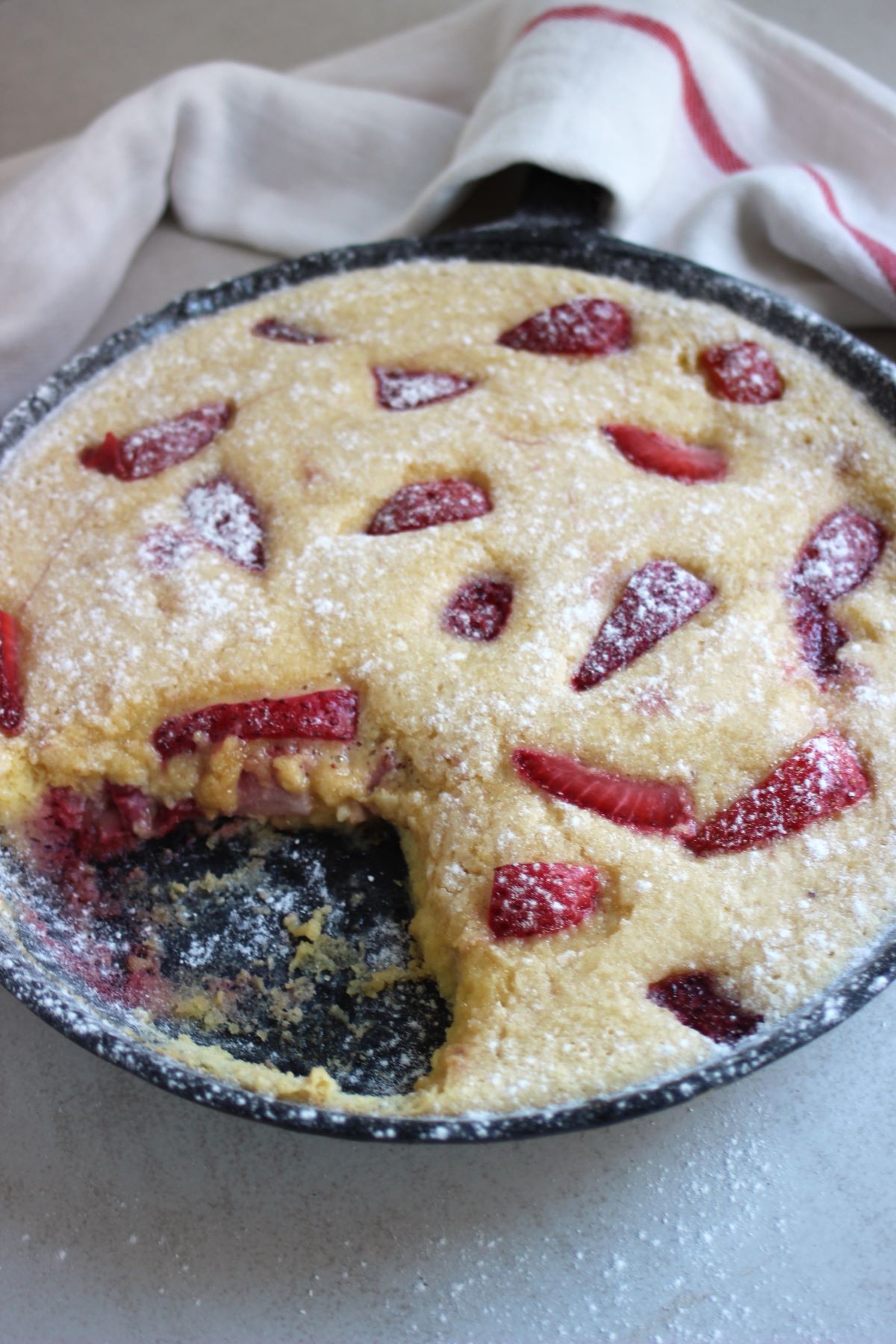 Strawberry clafoutis, without a piece, in a black skillet.