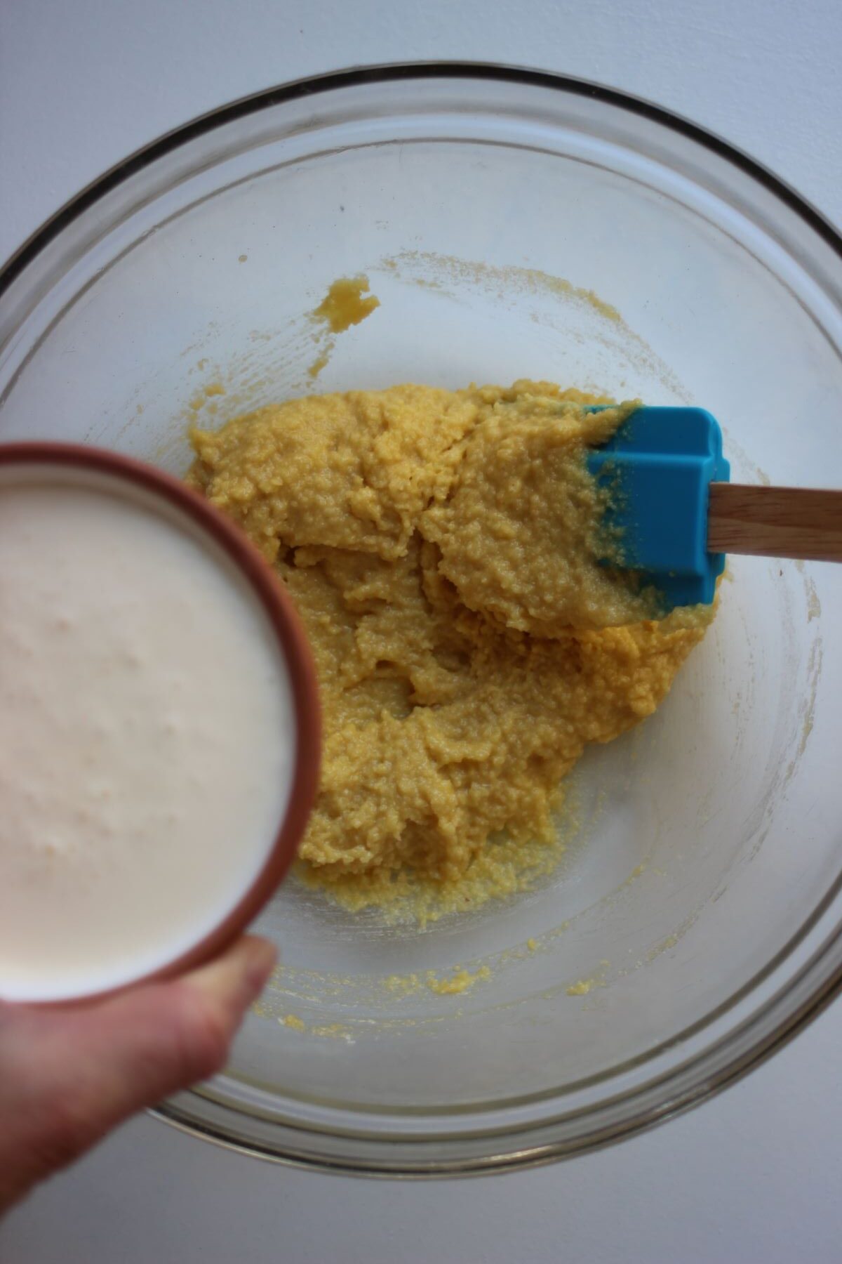 Bowl with cream is about to be poured into glass bowl with yellow mixture.