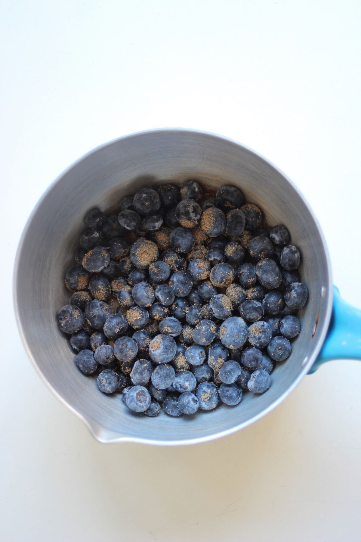 A deep saucepan with blueberries and brown sugar seen from above.