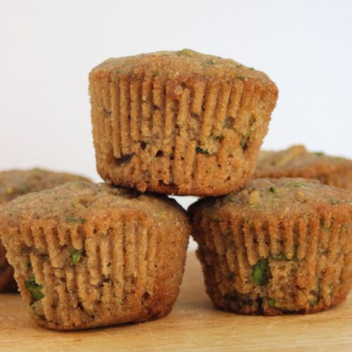 Zucchini muffins on a wooden board. More muffins behind.