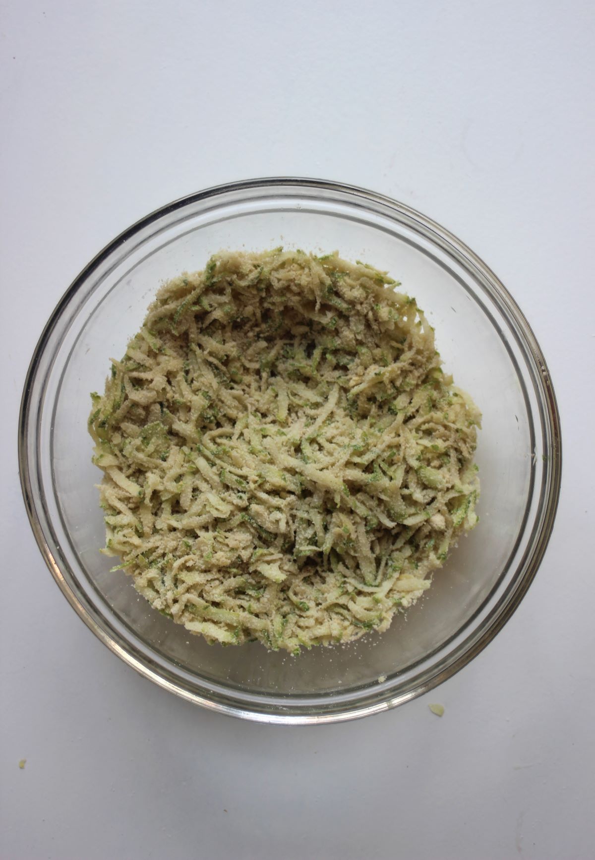 Glass bowl with a mixture of grated zucchini and flours.