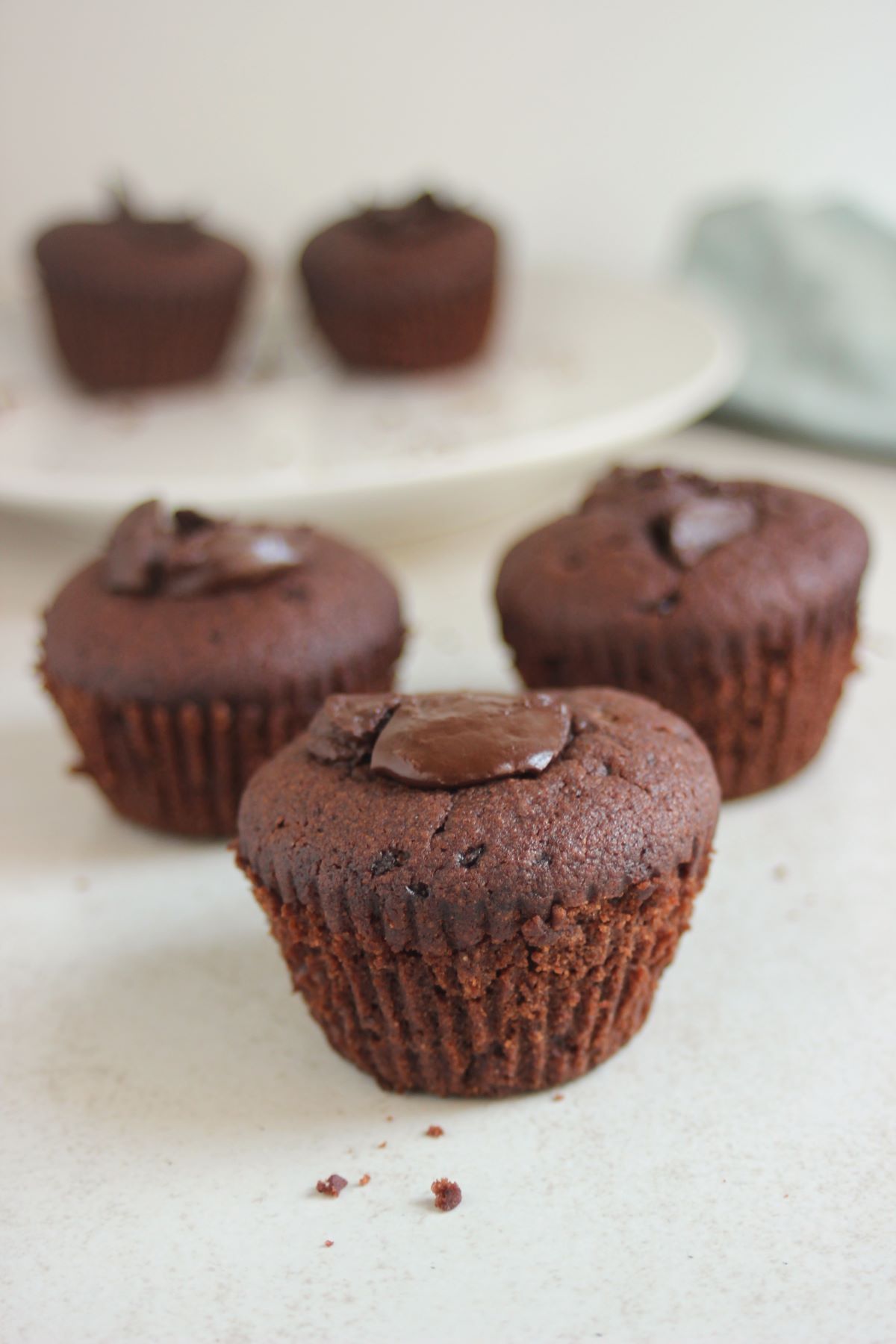 Chocolate muffins on a white surface. More muffins on the background.