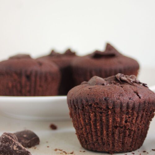 Chocolate muffin on a white surface. More muffins in a white plate on the background.