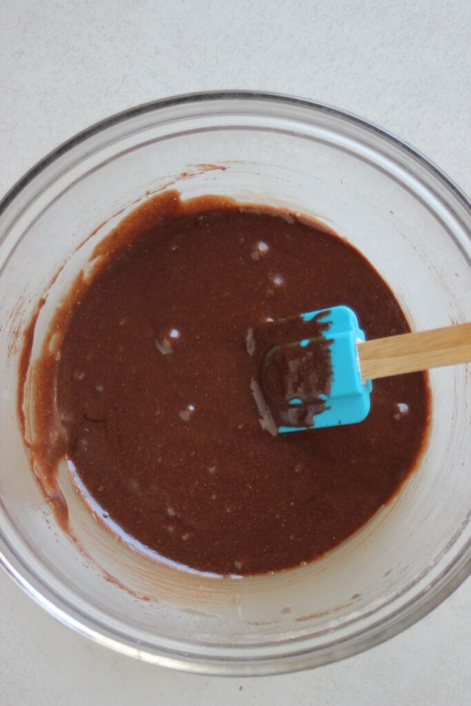Glass bowl with a brown mixture and a rubber spatula.