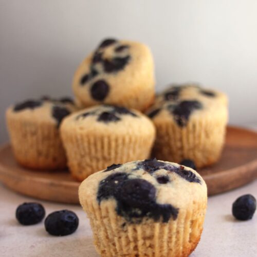 Blueberry muffin on a white surface. More muffins behind on a wooden plate.