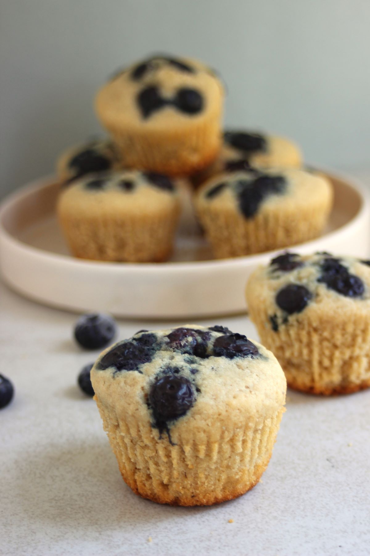 Blueberry muffin on a white surface. More muffins behind.