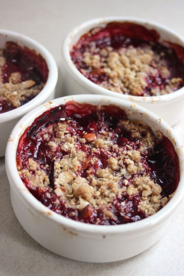 Three ramekins with plum crisp on a white surface.