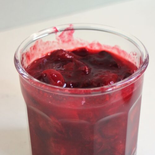 Jar with plum sauce on a white surface.