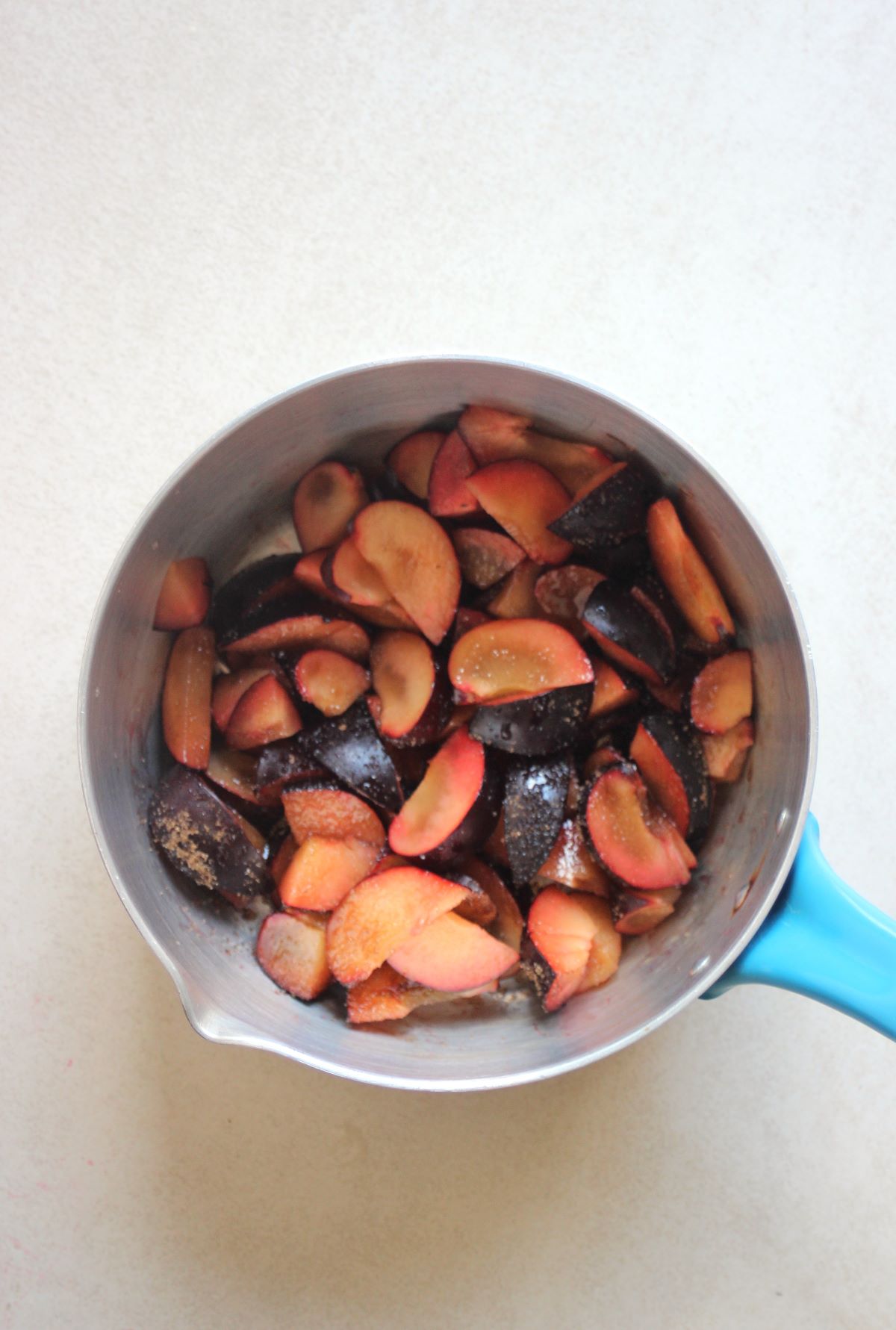 Deep saucepan with sliced plums and brown sugar.