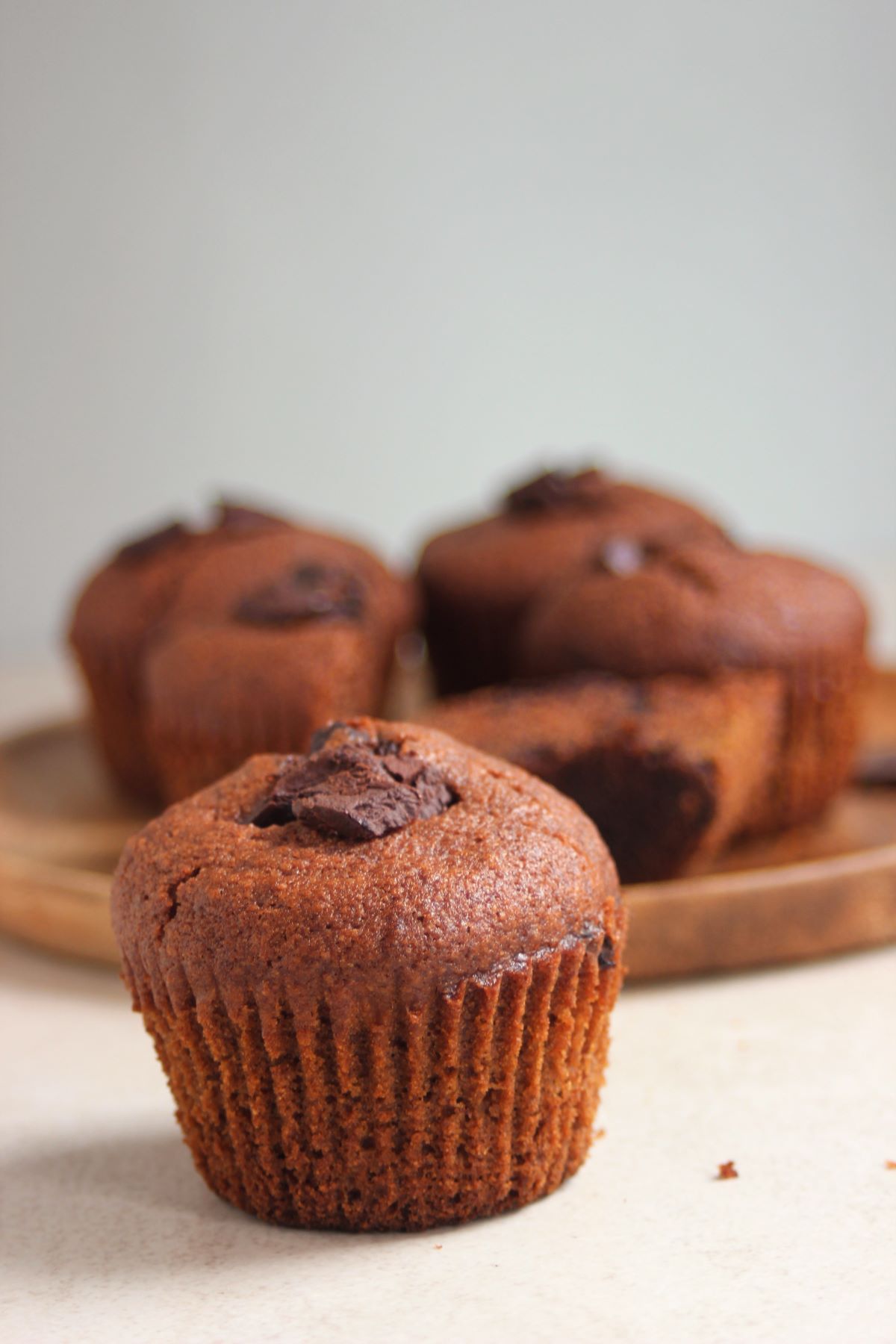 A chocolate banana muffin, and more muffins behind on a wooden plate.